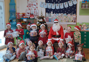 Dzieci z grupy Misie pozują do zdjęcia z Mikołajem, w rękach trzymają prezenty.