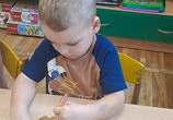 Chłopiec siedzi przy stoliku i dekoruje pisakami lukrowymi swoje ciasteczka.
