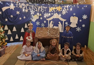 Dzieci z grupy Misie pozują do zdjęcia na tle dekoracji świątecznej w strojach jasełkowych.
