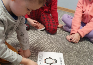 Chłopiec z grupy „Liski” siedząc na dywanie układa napis – pingwin.