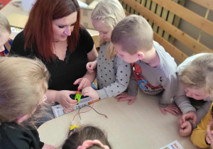 Wychowawczyni wraz z dziećmi buduje obwód elektryczny, dzięki któremu dioda w kontrolce się zaświeci.