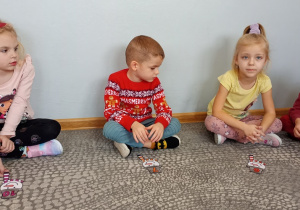 Dzieci siedzą przed postacią bałwanka z zapisaną cyfrą na kapeluszu.