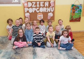 Dzieci z grupy Słoneczka siedzą pod tablicą z napisem Dzień Popcornu.