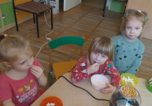 Trzy dziewczynki siedzą przy stoliku i zajadają zrobiony popcorn