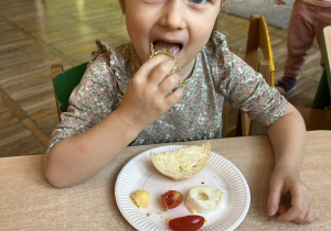 Dziewczynka je kanapkę z jajkiem, pomidorem i kiełkami brokułu.