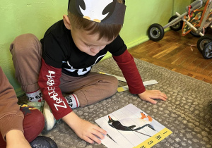Chłopiec układa na dywanie puzzle ze zdjęciem pingwina.