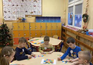 Dzieci siedzą przy stoliku i układają puzzle z klocków Lego według podanego wzoru.