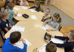 Przedszkolaki siedzą przy stolikach i wykonują kartę pracy – łączą w pary klocki.
