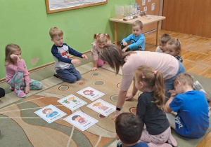 Nauczyciel prezentuje dzieciom na dywanie karty demonstracyjne przedstawiające zmysły.