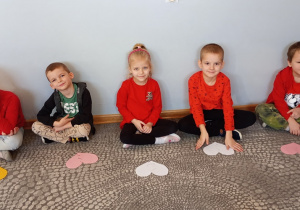 Przedszkolaki siedzą na dywanie z ułożonymi połówkami serc.