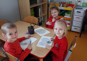 Trójka dzieci siedzi przy stoliku i koloruje mandale w kształcie serca.