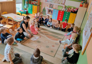 Dzieci z grupy Misie siedzą na dywanie i słuchają historii pizzy przedstawianą przez panią nauczycielkę.