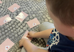 Chłopiec układa serduszko z odpowiednią cyfrą na kopercie walentynkowej.