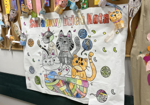 Na tablicy z pracami dzieci wiszą wykonane przez nie kotki oraz pokolorowana duża kolorowanka.