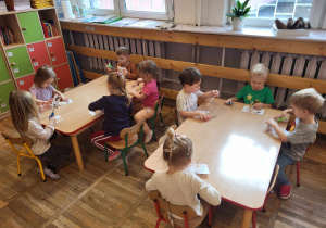 Dzieci siedzą przy stolikach, wycinają puzzle kota po śladzie.