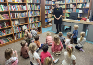 Dzieci siedzą na dywanie, pani Monika opowiada o bibliotece.