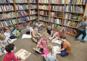 Dzieci siedzą na dywanie, oglądają samodzielnie wybrane książki.