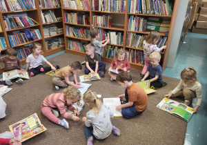 Dzieci siedzą na dywanie, oglądają samodzielnie wybrane książki.