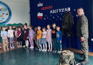 Dzieci z grupy „Odkrywcy” na tle dekoracji śpiewają dla żołnierzy Pieśń Reprezentacyjną Wojska Polskiego.
