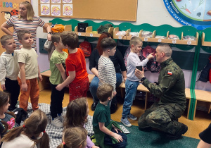 Żołnierz maluje chętnym dzieciom twarze farbkami maskującymi.