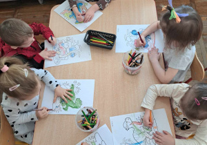Dzieci kolorują obrazki przedstawiające dinozaury przy stoliku.