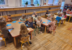 Dzieci siedzą przy stolikach, wypełniają białą plasteliną rysunek zęba.