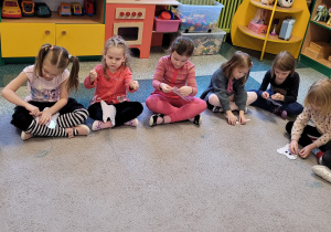 Dzieci z grupy Motylki siedzą na dywanie i przewlekają przez dziurki w sylwecie zęba sznurek.