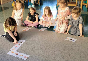Dziewczynki z grupy Motylki grają na dywanie w domino.