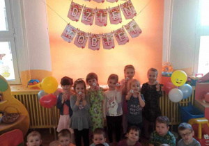 Dzieci z grupy Żabki pozują do zdjęcia na tle dekoracji z okazji Dnia Kobiet.