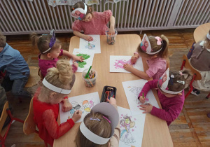 Dziewczynki z grupy Biedronki w opaskach na głowie, kolorują obrazki z okazji Dnia Kobiet.