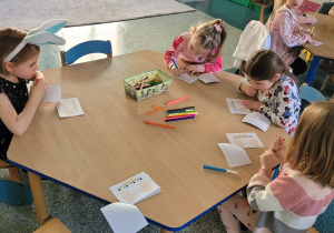 Dziewczynki siedzą przy stoliku i malują paznokcie według rytmu.