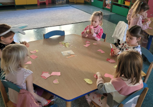 Dziewczynki siedzą przy stoliku i wycinają elementy do pracy plastycznej.