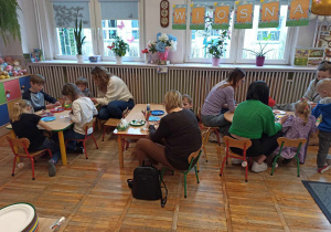 Dzieci z grupy Biedronki wraz z rodzicami siedzą przy stoliczkach, wspólnie tworząc ozdoby wielkanocne.