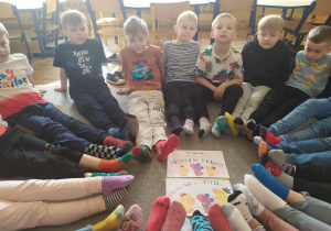 Dzieci siedzą w kole na dywanie i prezentują swoje skarpetki nie do pary, w których przyszły do przedszkola.