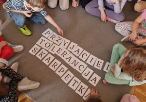 Na dywanie są ułożone hasła „przyjaciel”, „tolerancja”, „skarpetka”. Dzieci siedzą wokół haseł.