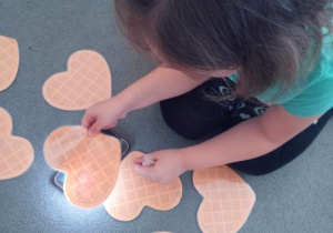 Dziewczynka siedzi na dywanie i podświetla obrazek gofra by dowiedzieć się jaki dodatek się na nim ukrył.
