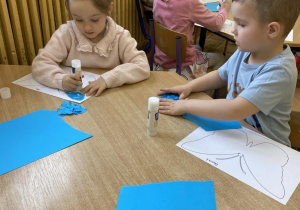 Dzieci z grupy Słoneczka wyklejają na niebiesko motyla.