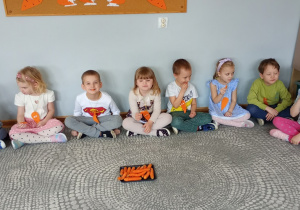Dzieci siedzą na dywanie i kosztują marchewki.
