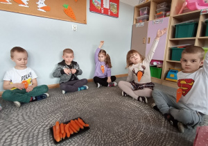 Dzieci siedzą na dywanie i omawiają walory odżywcze marchewek.