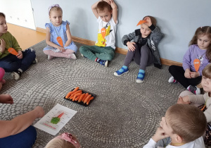 Przedszkolaki siedzą na dywanie i podają przykłady potraw z wykorzystaniem marchewek.