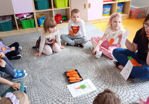 Nauczycielka prezentuje dzieciom zajączka z cyfrą na brzuszku i papierową marchewką.