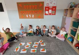 Przedszkolaki prezentują marchewki trzymane w dłoniach.