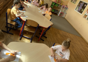 Dzieci siedzą przy stoliku i wykonują pracę plastyczną z użyciem plasteliny.