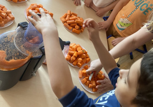 Chłopiec wkłada do sokowirówki pokrojoną marchewkę.