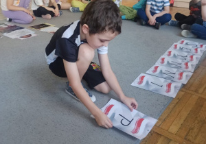 Chłopiec z grupy układa na dywanie literę do napisu Słynni Polacy.