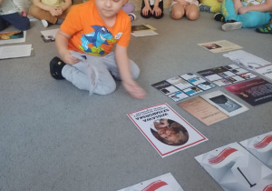 Chłopiec układa na dywanie zdjęcie oraz informacje dotyczące Wisławy Szymborskiej.