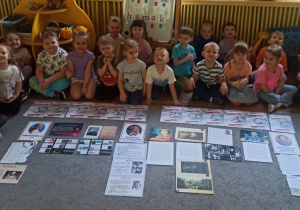 Cała grupa pozuje do zdjęcia z przygotowaną na dywanie wystawą o Słynnych Polakach.