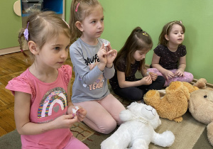 Dziewczynki siedzące na dywanie uczą się jak prawidłowo przykleić plaster na ranę.