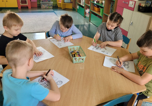 Chłopcy i dziewczynka siedzą przy stoliku i kolorują obrazek.