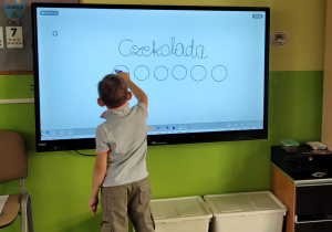 Chłopiec stoi przy ekranie i zamalowuje kółeczka zgodnie z ilością sylab w wyrazie.